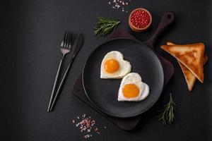 deux œufs frits en forme de coeur sur une plaque en céramique noire sur un fond de béton foncé photo