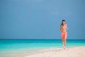 Monter la jeune femme faisant des exercices sur la plage blanche tropicale dans ses vêtements de sport photo