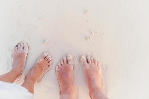 gros plan des pieds de la famille sur la plage de sable blanc photo