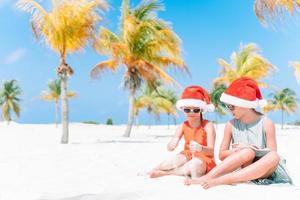 petites filles adorables en chapeaux de père noël pendant les vacances à la plage s'amuser ensemble photo