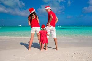 famille heureuse de trois personnes en chapeaux de noël pendant les vacances tropicales photo