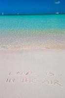 l'amour est dans l'air écrit sur le sable blanc de la plage tropicale photo