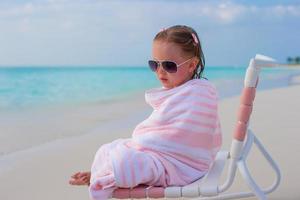 adorable petite fille recouverte d'une serviette assise sur une chaise de plage photo