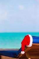 chaise longue avec bonnet de noel sur une belle plage tropicale avec sable blanc et eau turquoise. vacances de noël parfaites photo