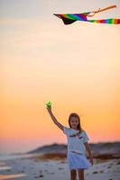 petite fille avec cerf-volant sur la plage tropicale au coucher du soleil. enfant joue sur le rivage de l'océan. enfant avec des jouets de plage. photo