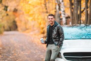 jeune homme buvant du café avec téléphone dans le parc d'automne à l'extérieur photo