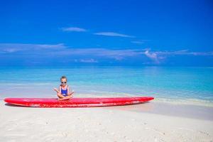 petite fille s'amuser sur une planche de surf sur une plage tropicale photo