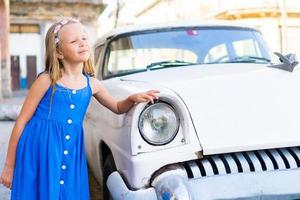 adorable petite fille dans un quartier populaire de la vieille havane, cuba. portrait d'enfant arrière-plan voiture américaine classique vintage photo