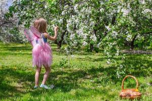 adorable petite fille avec un panier de paille dans un verger de pommiers en fleurs photo