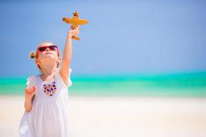 bonne petite fille avec un avion jouet dans les mains sur la plage de sable blanc. publicité photo de voyage, vols et compagnies aériennes