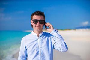 jeune homme avec ordinateur portable et téléphone sur le fond de l'océan turquoise à la plage tropicale photo