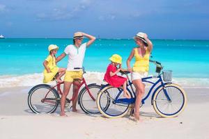 jeune famille de quatre personnes faisant du vélo sur une plage de sable tropicale photo