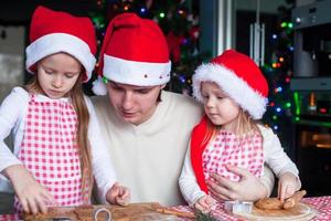 petites filles avec jeune papa en bonnet de noel cuire des biscuits de pain d'épice de noël photo