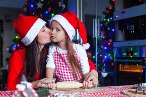 adorable petite fille avec sa mère portant des chapeaux de père noël préparant des biscuits de pain d'épice de noël ensemble photo