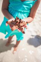 petite fille adorable avec des étoiles de mer dans les mains à la plage tropicale photo