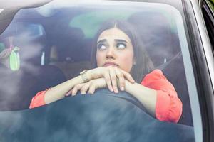 femme stressée conductrice assise à l'intérieur de sa voiture. conductrice en colère au volant d'une voiture. jeune femme en colère coincée dans un embouteillage. femme agacée en voiture. fille coincée dans la circulation. photo