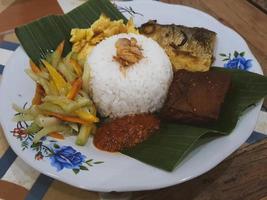 une portion de nasi kucing avec tête de chanos frite, tofu, servie sur une assiette avec des feuilles de bananier. photo