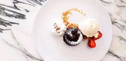 plat ou vue de dessus du gâteau de lave au chocolat avec glace à la vanille, crème fouettée et tranches de fraise dans une assiette sur une table en marbre blanc. concept de dessert et de nourriture sucrée photo