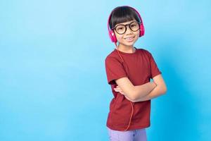 thai asie fille enfant écoutant de la musique, portant des écouteurs phink sur studio bleu sur fond bleu