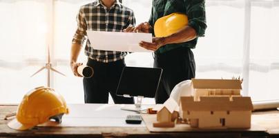 bureau d'ingénieur avec papier objet et tablette avec travail d'équipe d'ingénieurs flous travaillant dur pour consulter sur leur projet de construction. photo