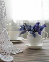un bouquet de fleurs de muscari dans un vase blanc sur une table près de la fenêtre. printemps nature morte