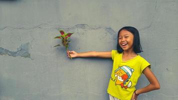 petite fille tenant une jeune plante. feuilles vertes. notion d'écologie. fond de couleur claire. photo