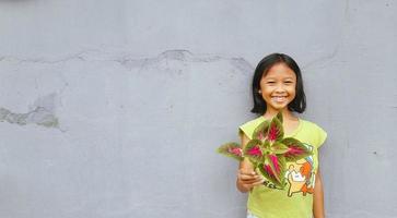 petite fille tenant une jeune plante. feuilles vertes. notion d'écologie. fond de couleur claire. photo