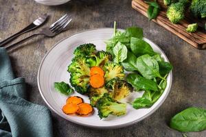 brocoli et carottes grillés et feuilles d'épinards frais sur une assiette. régime végétal. photo