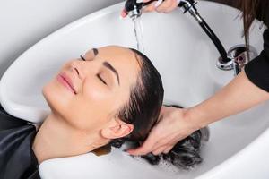 coiffeur professionnel laver les cheveux d'une jeune femme dans un salon de beauté photo