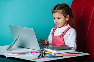 jolie petite fille utilisant un ordinateur portable à la maison. concept de retour à l'école. la fille fait ses devoirs seule sur l'ordinateur portable photo