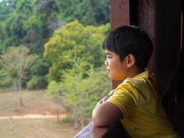 garçon regardant par la fenêtre en regardant la forêt verte photo