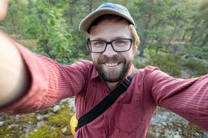 un homme heureux et souriant dans une casquette et des lunettes fait un selfie, sur le fond de la forêt. loisirs. photo