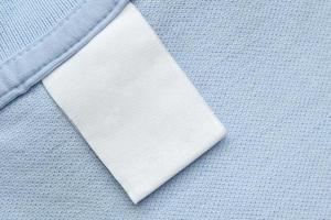 étiquette blanche de vêtements de soin de blanchisserie vierge sur fond de tissu de chemise bleue photo