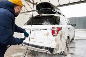 homme lavant une voiture suv américaine à eau haute pression avec galerie de toit au lavage en libre-service par temps froid. photo