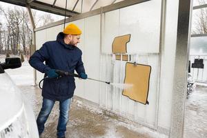 homme lavant des tapis de voiture à haute pression au lavage en libre-service par temps froid. photo