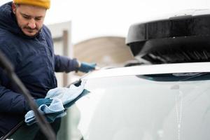 l'homme essuie le pare-brise de la voiture suv américaine avec un chiffon en microfibre après le lavage par temps froid. photo