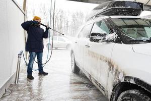 homme lavant une voiture suv américaine à eau haute pression avec galerie de toit au lavage en libre-service par temps froid. photo