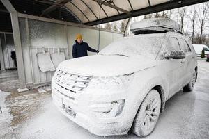 homme lavant une voiture suv américaine avec galerie de toit lors d'un lavage en libre-service par temps froid. photo