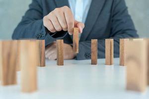 l'assurance avec les mains protège le domino. les mains de l'homme d'affaires empêchent les dominos de tomber dans la crise des affaires. contrôle des risques commerciaux et planification et stratégies pour gérer les entreprises d'assurance. photo