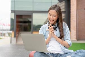 belle femme asiatique étudiante excitée vérifiant les résultats des tests de langue sur ordinateur portable. sourire fille heureuse étude en ligne. réserver sur le campus universitaire. portrait féminin sur l'université internationale d'asie. photo