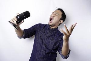 portrait d'un homme asiatique insouciant, s'amusant au karaoké, chantant au microphone en se tenant debout sur fond blanc photo