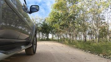 à côté d'une voiture grise roulant sur une route de terre. avec la nature de l'herbe verte et des hévéas sous le ciel bleu. photo