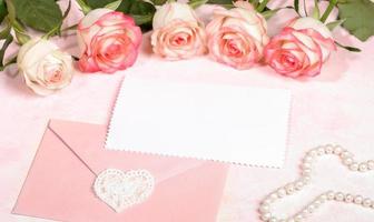 maquette festive avec roses roses, enveloppe avec coeur en dentelle, feuille blanche vide, perles de nacre sur rose. photo