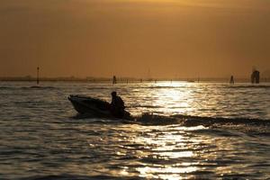 silhouette de pêcheur au coucher du soleil dans le port de chioggia lagune de venise depuis un bateau photo