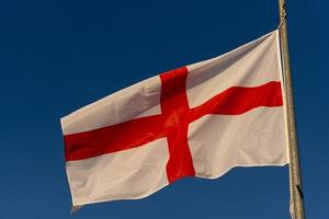 agitant le drapeau anglais croix rouge sur blanc isolé sur bleu photo