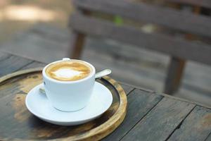 café chaud avec mousse florale dans une tasse blanche fond bois gris photo
