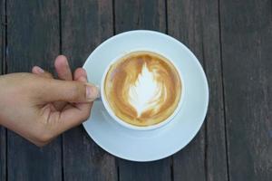 café chaud dans des mains humaines. fleurs de mousse de café dans une tasse blanche. fond de bois gris photo