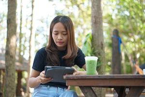 les femmes asiatiques sont heureuses de s'asseoir et de travailler dans un café. il y a des arbres verts entourés par la nature. la planification d'entreprise est une bonne idée. photo