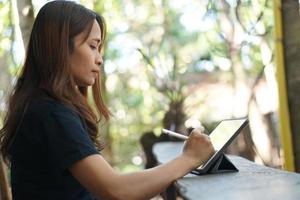 les femmes asiatiques sont heureuses de s'asseoir et de travailler dans un café. il y a des arbres verts entourés par la nature. la planification d'entreprise est une bonne idée. photo