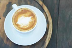 café chaud avec mousse florale dans une tasse blanche fond bois gris photo